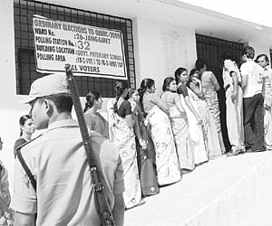 A cop keeps a vigil as voters queue up to exercise their franchise during the GHMC elections at a polling booth in Ravindra Naik Nagar of Jangampet di