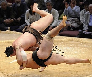 Grand champion Hakuho (top) sends champion Kotooshu to the dirt in their bout at Fukuoka, southern Japan, on Friday Nov. 27, 2009. (AP)