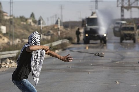 a Palestinian uses a sling shot to throw stones towards Israeli soldiers during clashes in Jalazoun Refugee Camp, near the West Bank city of Ramallah. |AP