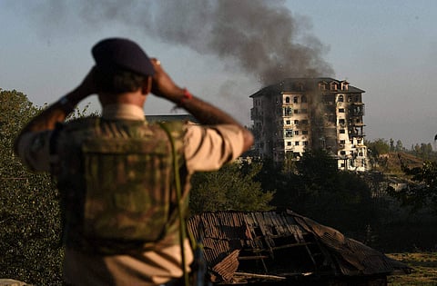 A security officer watching through the binocular at multi-storied government building where some militants are holed up at Pampore 16 kms from Srinagar on Tuesday. | PTI