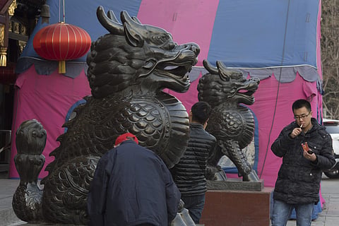 a Chinese man lights up outside a restaurant with stone mythical creatures statues in Beijing | AP
