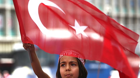 A Turkish girl wearing a headband bearing the name of Turkish president Recep Tayyip Erdogan waves her nation flags during a pro-government demonstration.