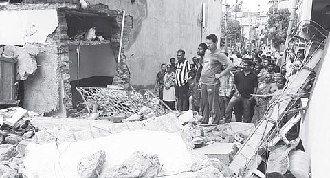 Onlookers gather at the site after the building came crashing down following cylinder leak at Ejipura on Monday (EPS | Nagesh Polali)