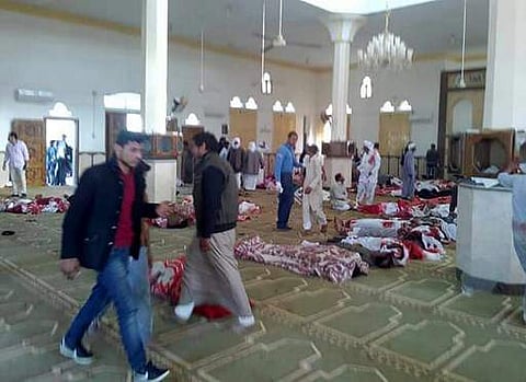 Egyptians walk past bodies following a gun and bombing attack at the Rawda mosque, roughly 40 kilometres west of the North Sinai capital of El-Arish, on November 24, 2017. | AFP