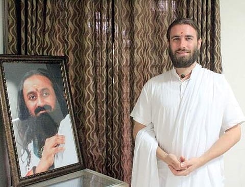 Swami Purnachaitanya besides a photograph of Sri Sri Ravi Shankar Jainth Thomas Joseph