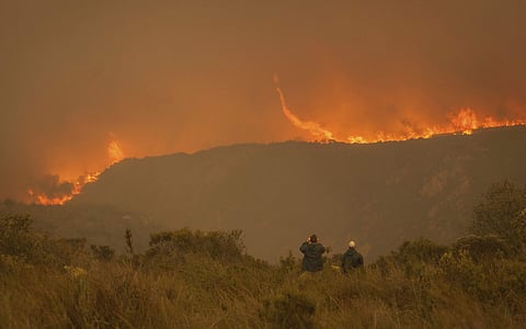 In this photo taken Wednesday, June 7, 2017, onlookers watch a blaze in the Kranshoek area of South Africa. (AP)