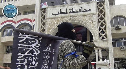 A fighter from Syria's al-Qaida-linked Nusra Front holds his group flag as he stands in front of the governor building in Idlib province, north Syria (File | AP)