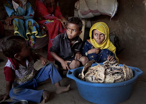 In this Oct. 1, 2018, photo, children sit in front of moldy bread in their shelter, in Aslam, Hajjah, Yemen. In a plastic washtub, the children's mother collects hard bread crumbs even those covered with mold, then mix with water, add salt, and give to h