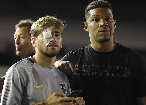 Wearing an eye patch, Gonzalo Lamardo, left, and Wilmar Barros of Argentina's Boca Juniors, walk on the pitch of the Antonio Vespucio Liberti stadium, after the final soccer match of the Copa Libertadores was rescheduled for Sunday, in Buenos Aires, Argen