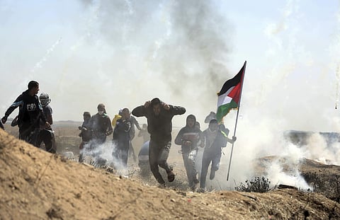 Palestinian protesters run for cover from teargas fired by Israeli troops during a protest at the Gaza Strip's border with Israel, Friday, April 6, 2018. | AP