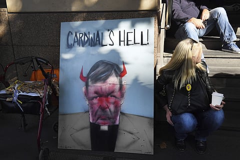 A demonstrator sits beside a placard carrying the image of Australian Cardinal Greorge Pell, outside the Melbourne Magistrate Court in Melbourne Tuesday, May 1, 2018. (AP)