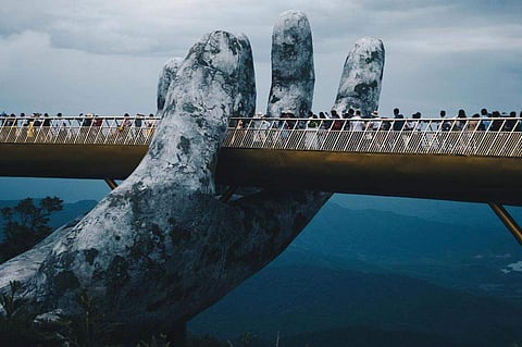 Nestled in the forested hills of central Vietnam two giant concrete hands emerge from the trees, holding up a glimmering golden bridge. (Photo | AP)