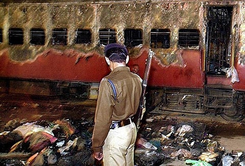 A policeman looks over a burnt coach and belongings of Hindu activists at Godhra station, on 28 February 2002, some 200 kms from Ahmadabad. (File | AFP)