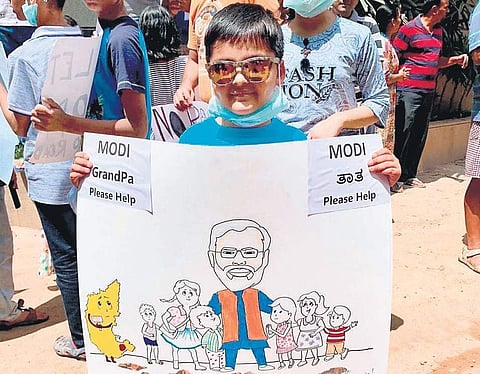 A kid holds a placard reading ‘Modi Grandpa, please help’ urging the Prime Minister to look into the sorry state of roads in HN Halli ( Photo | EPS )
