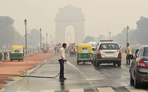 A worker sprays water on a road under heavy smog conditions in New Delhi on November 13 2019. | (Photo | Parveen Negi/EPS)