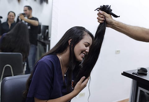 Valery Díaz holds the hair she had cut off to earn $100 in Caracas, Venezuela, Friday, April 5, 2019. After a drastic cut of 60 centimeters that was reduced to less than two, Díaz looked silently into the mirror at what hair remained, as her mother encour