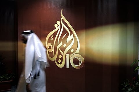 A Qatari employee of Al Jazeera Arabic language TV news channel walks past the logo of Al Jazeera in Doha.