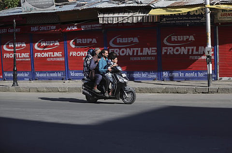 A Kashmiri family rides on a scooter past a closed market in Srinagar (Photo | AP)