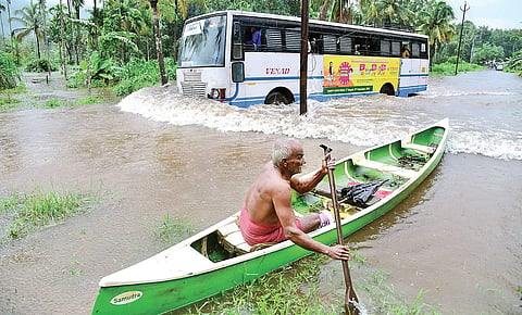 A man manoeuvring his boat through the flooded Kothamangalam-Kuttampuzha road as a KSRTC bus passes by at Nyayapalli near Kuttumpuzha on Thursday | Albin Mathew