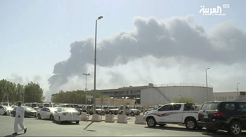In this image made from a video broadcast on the Saudi-owned Al-Arabiya satellite news channel on Saturday, Sept. 14, 2019, a man walks through a parking lot as the smoke from a fire at the Abqaiq oil processing facility can be seen behind him in Buqyaq,