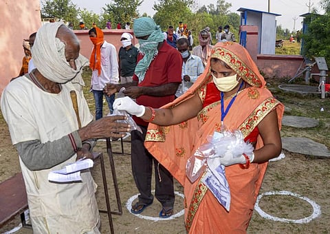 A polling official distributes gloves among voters as they wait to cast their votes for the first phase of Bihar Assembly Election. (Photo | PTI)