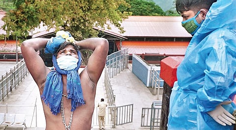 A devotee offers prayers at the Sabarimala temple on Monday as a policeman in PPE kit watches | Shaji Vettipuram