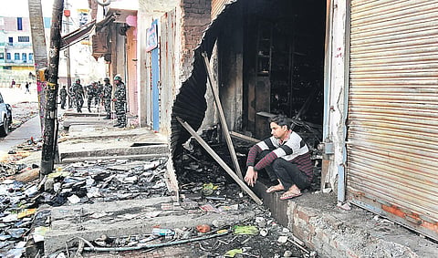 Security forces are seen in a riot-hit street in northeast Delhi as a youth sits outside a gutted shop. ( Photo | Parveen Negi, EPS)