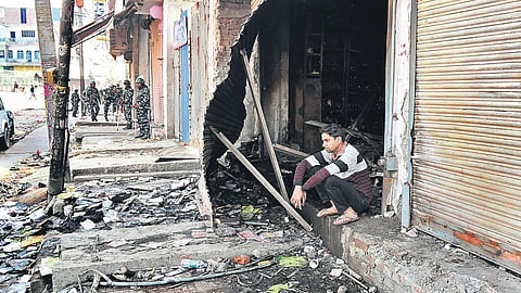 Security forces are seen in a riot-hit street in northeast Delhi as a youth sits outside a gutted shop.