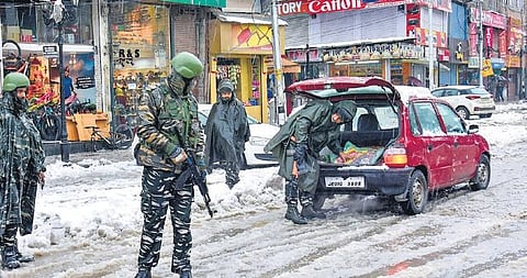 A security personnel checks a vehicle as others stand guard during snowfall in Srinagar on Monday. (Photo | PTI)