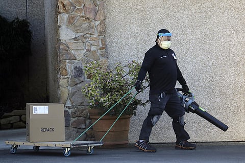 A worker at the Life Care Center in Kirkland, Wash., wears a mask and uses a leaf blower as he wheels a package on a cart. The nursing home is at the center of the outbreak of the coronavirus in Washington state. (Photo | AP)