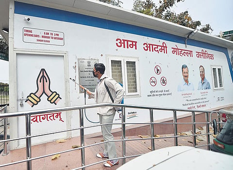 A worker sprays disinfectants on a mohalla clinic at IP Extension. (Photo | PTI)