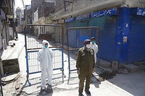 Pakistan volunteers and a police officer stand guard outside the area which authorities sealed after a group of people tested positive for the new coronavirus. (File Photo | AP)