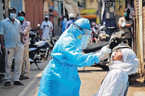 A medic collects swab from the mouth of a woman resident for COVID-19 test in a containment zone in Mumbai. (Photo | PTI)