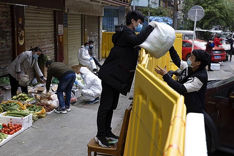 A vendor hands over grocery to another across barriers used to seal off a neighborhood to help curb the spread of the coronavirus in Wuhan, China, Friday, April 3, 2020. (Photo | AP)