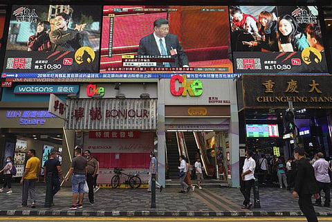 Pedestrians walk under a giant screen showing live telecast of Chinese President Xi Jinping, top center, at the closing session of the National People's Congress, in Hong Kong, Thursday, May 28, 2020. China’s ceremonial legislature on Thursday endorsed a