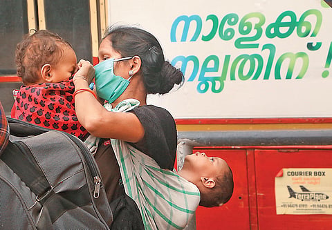 A woman covers her toddler’s face after coming out of a KSRTC bus on Kozhikode railway station premises, before boarding a special train to Jharkhand (Photo | TP Sooraj, EPS)