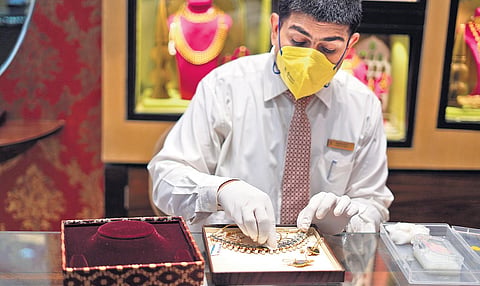 An attendant cleans a jewellery item before display at a Tanishq showroom after Unlock 1.0
