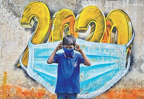 A boy puts on a mask while standing in front of graffiti done by artist Baadal Nanjundaswamy, in RT Nagar, Bengaluru. (PHOTO | SHRIRAM BN, EPS)