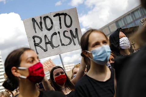 A woman shows a 'Stop Racism' sign as she attends a demonstration at the Alexander Platz in Berlin, Germany, Saturday, June 6, 2020, to protest against the recent killing of George Floyd by police officers in Minneapolis, USA, that has led to protests in