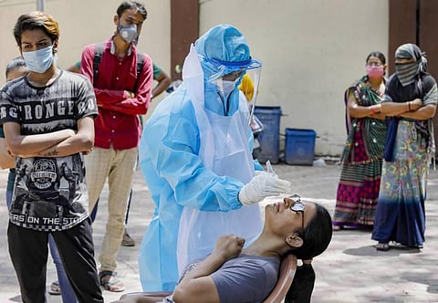 A healthcare worker wearing a PPE kit takes a sample of a woman for COVID-19 test at a residential area. (Photo | PTI)