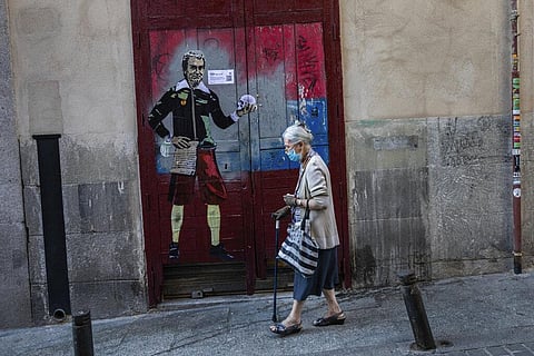 An elderly woman wearing a face mask to protect against the coronavirus walks past a painting named 'to be or not to be' by artist TVBOY. (Photo | AP)