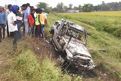 Villagers watch a burnt car which ran over and killed farmers on Sunday, at Tikonia village in Lakhimpur Kheri, Uttar Pradesh. (Photo | AP)