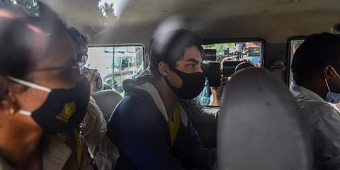 Shah Rukh Khan’s son Aryan Khan, center, escorted by law enforcement officials sits inside a vehicle outside NCB to appear before a court in Mumbai. (Photo | AP)