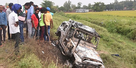 Villagers watch a burnt car which ran over and killed farmers on Sunday, at Tikonia village in Lakhimpur Kheri, Uttar Pradesh. (Photo | AP)