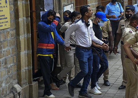 Bollywood actor Shah Rukh Khan’s son Aryan Khan, left, is escorted by law enforcement officials outside the Narcotics Control Bureau (NCB) to appear before a court. (Photo | AP)
