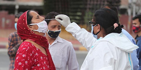 A health worker collects a swab sample of a woman to test for COVID- 19 at a market in Jammu. (Photo| AP)