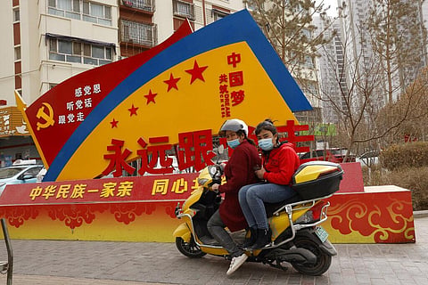 Residents wearing masks ride pass government propaganda in the city of Aksu in western China's Xinjiang region. (File Photo | AP)