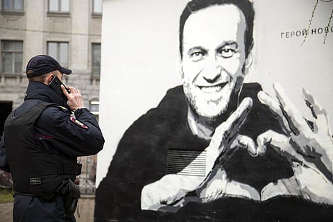 A police officer speaks on the phone near to graffiti of Russia's imprisoned opposition leader Alexei Navalny in St. Petersburg, Russia. (Photo | AP)