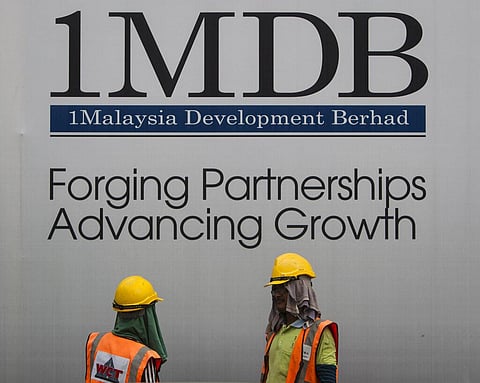 In this May 14, 2015, file photo, construction workers chat in front of a billboard for state investment fund 1 Malaysia Development Berhad (1MDB). (Photo | AP)