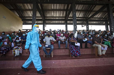 A Sri Lankan army soldier in protective suit walks past people waiting to receive a jab of Sinopharm COVID-19 vaccine. (Photo | AP)